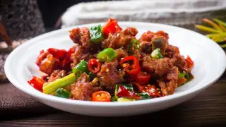 Chrupiący kurczak po kantońsku z papryczkami chili i zieloną cebulką na białym talerzu.