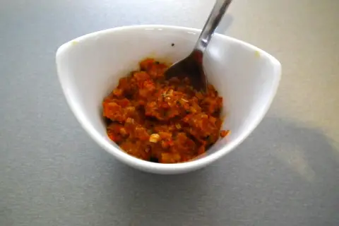 W białej miseczce znajduje się aromatyczna, czerwona pasta curry, gotowa do dodania smaku potrawom. Łyżeczka czeka, by nabrać jej porcję.