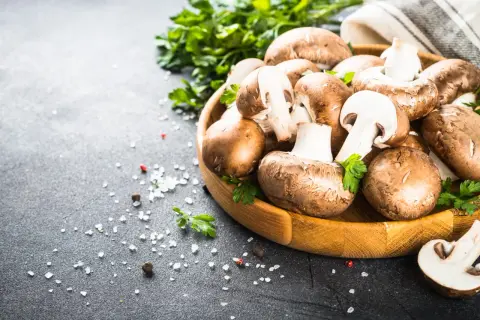 Drewniana miska z pieczarkami, natką pietruszki i solą na ciemnym tle.