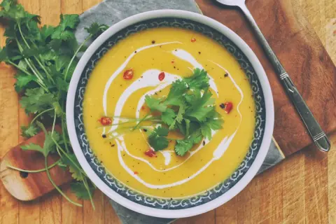 Aksamitna zupa dyniowa z mlekiem kokosowym, udekorowana świeżą kolendrą i chili. Idealna na chłodne dni.