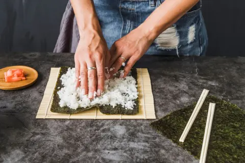 Ręce rozprowadzają ryż na nori, przygotowując się do zwinięcia sushi. Kluczowe jest, ile gotować ryż do sushi, by był idealny.
