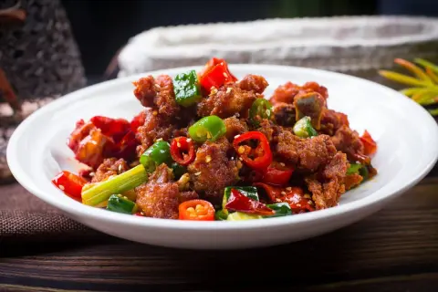 Chrupiący kurczak po kantońsku z papryczkami chili i zieloną cebulką na białym talerzu.