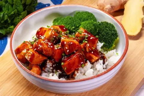 Aksamitny łosoś w sosie teriyaki, podany z ryżem i brokułami, posypany sezamem i szczypiorkiem. Pyszne danie gotowe do spożycia.