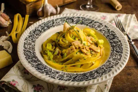 Pyszny kurczak curry z makaronem tagliatelle, podany na talerzu z ozdobnym wzorem. Obok czosnek i ser.