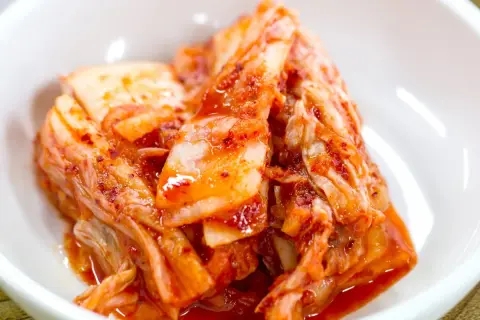 Domowe kimchi w białej miseczce, z widocznymi liśćmi kapusty i czerwoną przyprawą.
