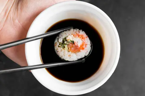Pałeczki trzymają sushi z łososiem, zanurzając je w miseczce gęstego słodkiego sosu do sushi.