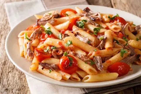 Penne z wieprzowiną i pomidorkami koktajlowymi, posypane natką pietruszki. Pyszne danie na obiad.
