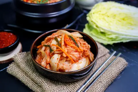 Miseczka z kimchi, pałeczki, miseczka z przyprawą i kapusta pekińska.