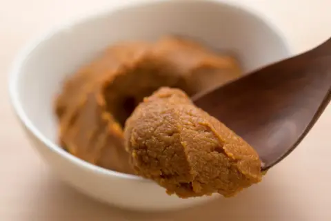 Łyżka nabiera porcję jasnej pasty miso z białej miseczki.