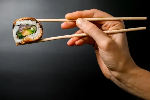 Dłoń trzyma pałeczkami jedno sushi. Zobacz, jak jeść sushi, by cieszyć się każdym kęsem!