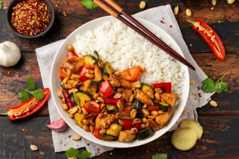 Pyszny kurczak kung pao z ryżem, papryką, cukinią i orzeszkami ziemnymi. Obok pałeczki, chili i czosnek.