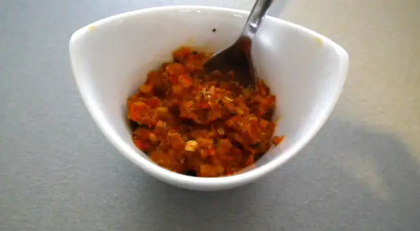 W białej miseczce znajduje się aromatyczna, czerwona pasta curry, gotowa do dodania smaku potrawom. Łyżeczka czeka, by nabrać jej porcję.