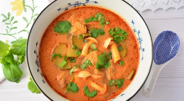 Aromaticzna zupa tom yum z kurczakiem, grzybami i kolendrą, podana w ozdobnej misce.