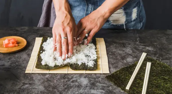Ręce rozprowadzają ryż na nori, przygotowując się do zwinięcia sushi. Kluczowe jest, ile gotować ryż do sushi, by był idealny.