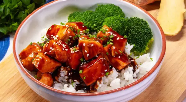 Aksamitny łosoś w sosie teriyaki, podany z ryżem i brokułami, posypany sezamem i szczypiorkiem. Pyszne danie gotowe do spożycia.