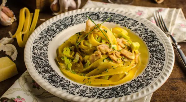 Pyszny kurczak curry z makaronem tagliatelle, podany na talerzu z ozdobnym wzorem. Obok czosnek i ser.