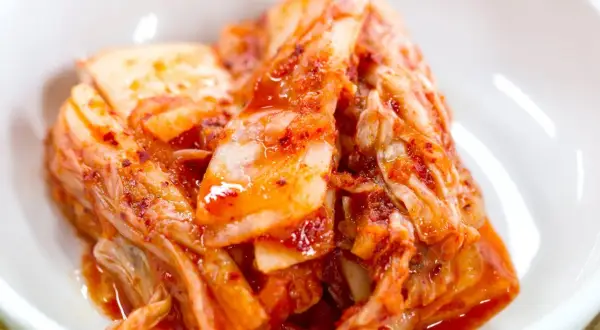 Domowe kimchi w białej miseczce, z widocznymi liśćmi kapusty i czerwoną przyprawą.