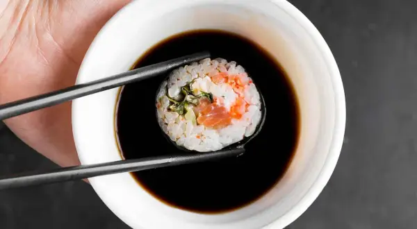 Pałeczki trzymają sushi z łososiem, zanurzając je w miseczce gęstego słodkiego sosu do sushi.