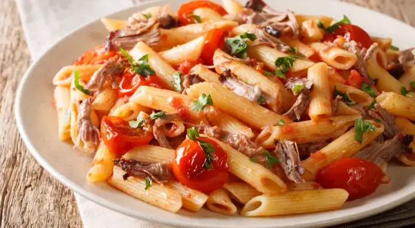 Penne z wieprzowiną i pomidorkami koktajlowymi, posypane natką pietruszki. Pyszne danie na obiad.