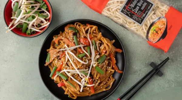 Pyszny makaron chow mein z kurczakiem, papryką i kiełkami fasoli mung, gotowy do podania. Obok paczka makaronu i miseczka z kiełkami.