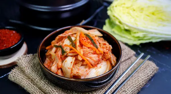 Miseczka z kimchi, pałeczki, miseczka z przyprawą i kapusta pekińska.