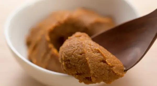 Łyżka nabiera porcję jasnej pasty miso z białej miseczki.