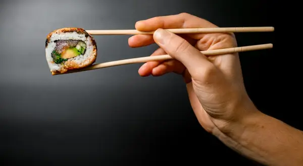 Dłoń trzyma pałeczkami jedno sushi. Zobacz, jak jeść sushi, by cieszyć się każdym kęsem!