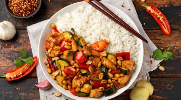 Pyszny kurczak kung pao z ryżem, papryką, cukinią i orzeszkami ziemnymi. Obok pałeczki, chili i czosnek.