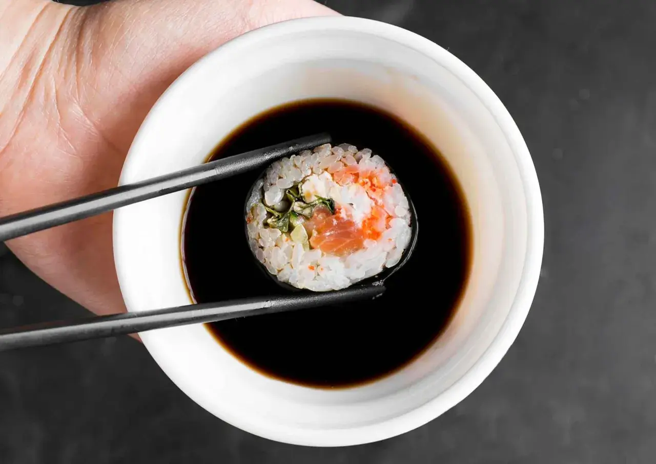 Pałeczki trzymają sushi z łososiem, zanurzając je w miseczce gęstego słodkiego sosu do sushi.