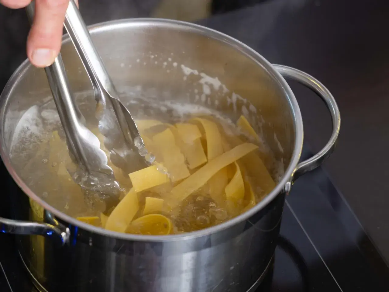 Szczypce wkładają szeroki makaron do wrzącej wody. Oto jak ugotować makaron krok po kroku.