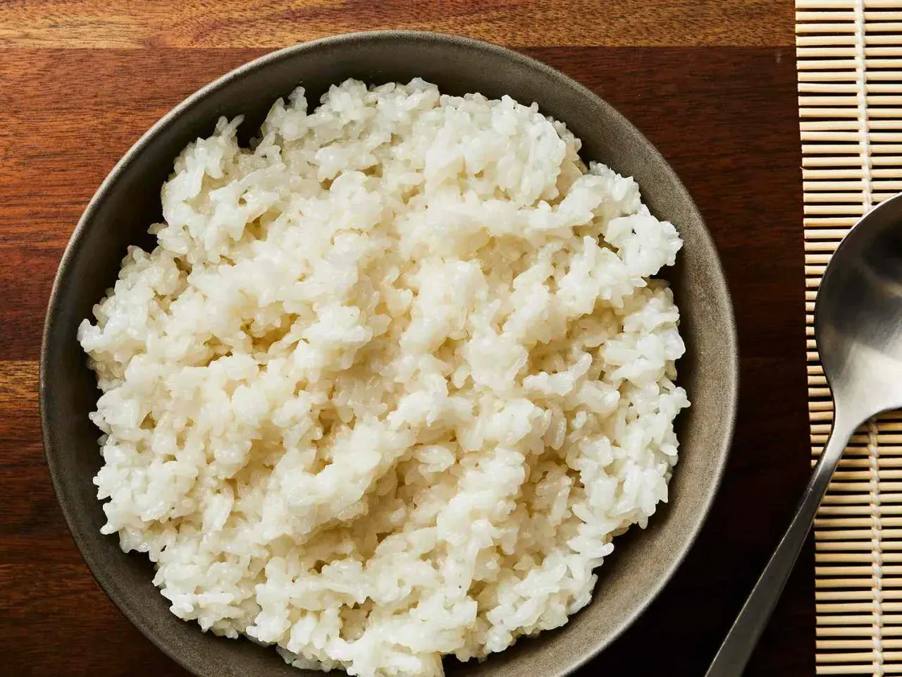 Idealny ryż do sushi: jak długo gotować, by był kleisty i puszysty. Miska pełna gotowego ryżu obok łyżki i maty bambusowej.