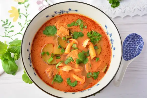 Aromaticzna zupa tom yum z kurczakiem, grzybami i kolendrą, podana w ozdobnej misce.