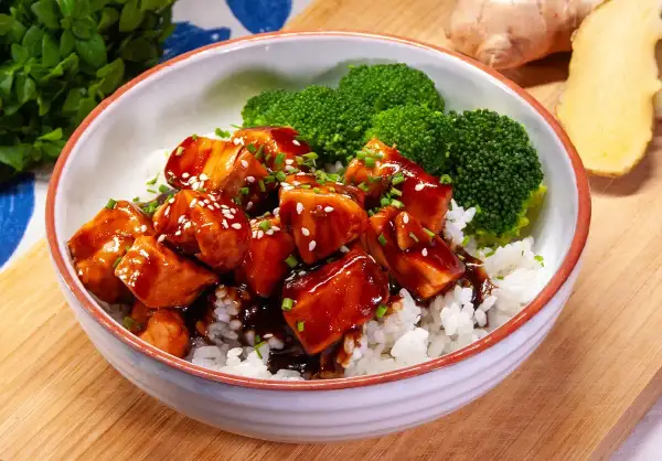 Aksamitny łosoś w sosie teriyaki, podany z ryżem i brokułami, posypany sezamem i szczypiorkiem. Pyszne danie gotowe do spożycia.