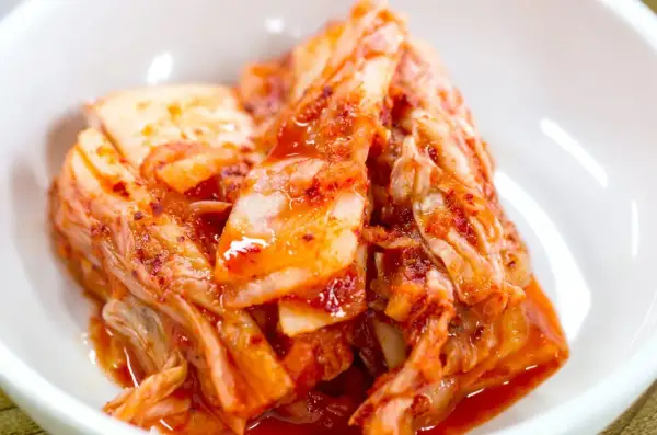 Domowe kimchi w białej miseczce, z widocznymi liśćmi kapusty i czerwoną przyprawą.