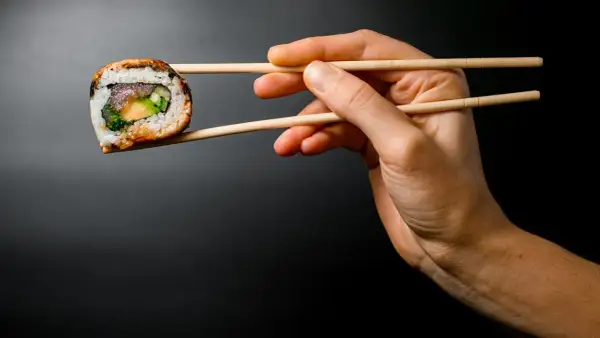 Dłoń trzyma pałeczkami jedno sushi. Zobacz, jak jeść sushi, by cieszyć się każdym kęsem!