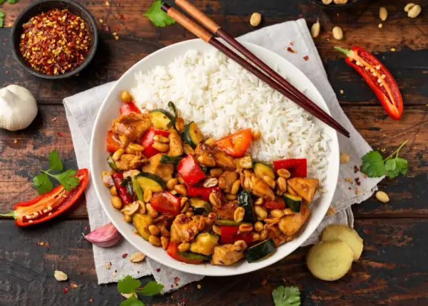 Pyszny kurczak kung pao z ryżem, papryką, cukinią i orzeszkami ziemnymi. Obok pałeczki, chili i czosnek.